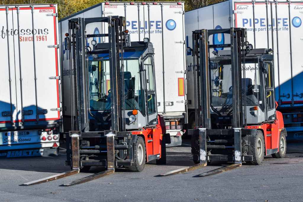 Två truckar uppställda bredvid varandra, ställda framför några lastbilssläp.